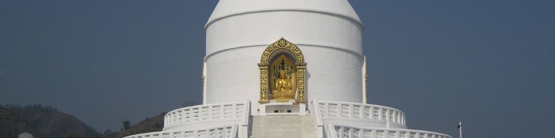 A white temple with a golden statue, surrounded by a white fence and a staircase leading to the entrance.