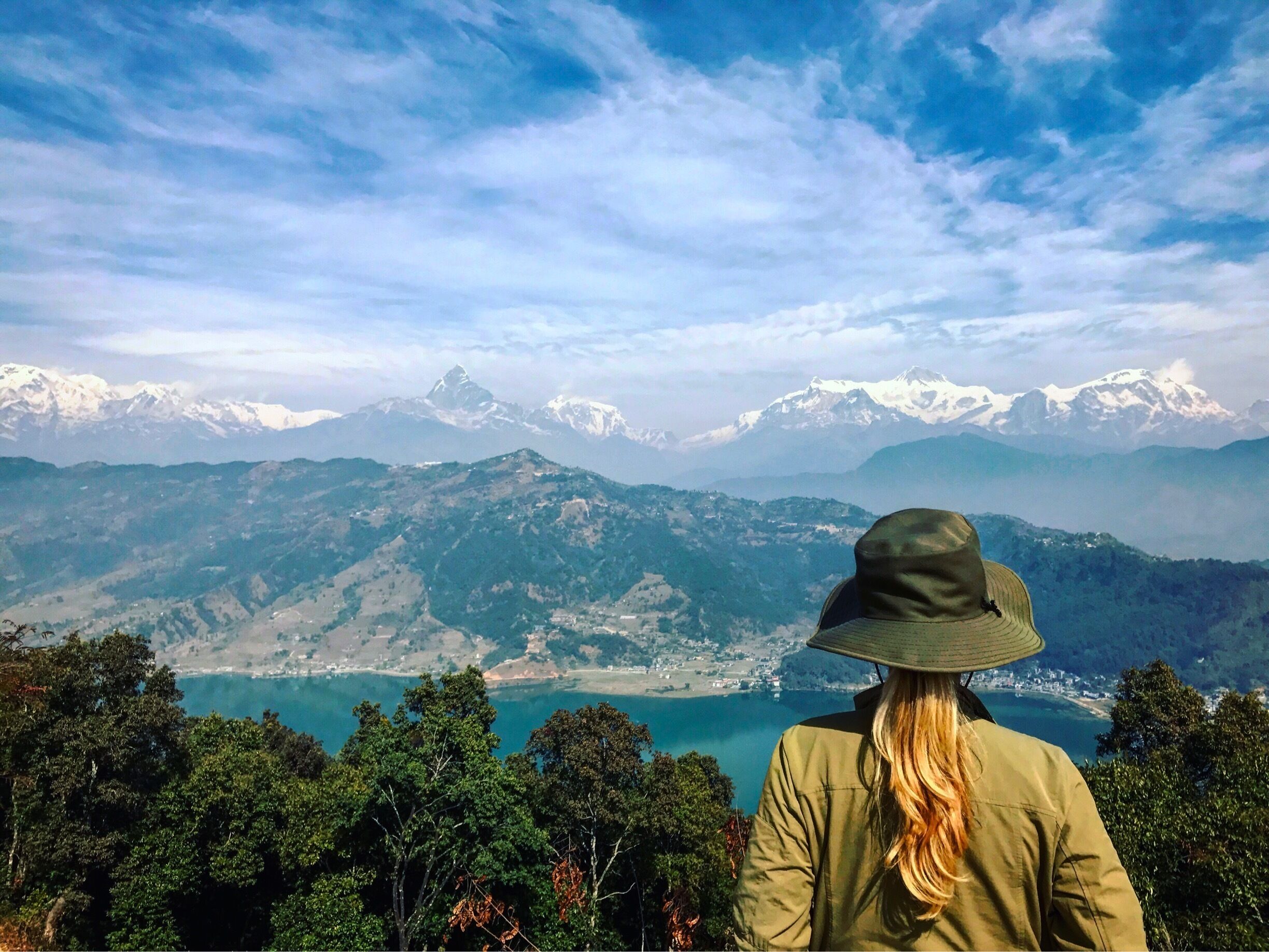 A person overlooking a mountainous landscape with a lake and snow-capped peaks in the distance.