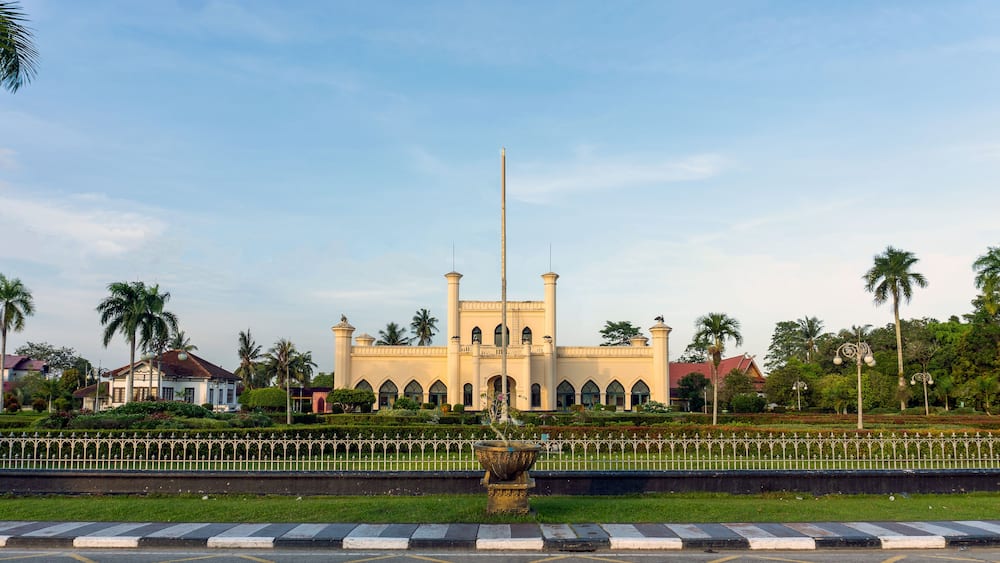 A large mosque with a tall minaret, surrounded by palm trees and a well-maintained garden.