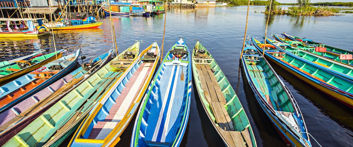 A row of colorful boats docked at a pier with buildings in the background.