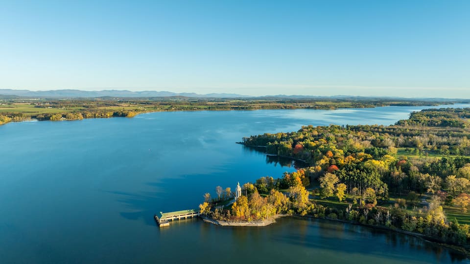 A large body of water with a dock, surrounded by autumn-colored trees and distant mountains.