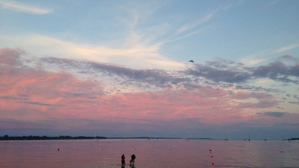 A sunset over a calm body of water with boats and people on the shore.