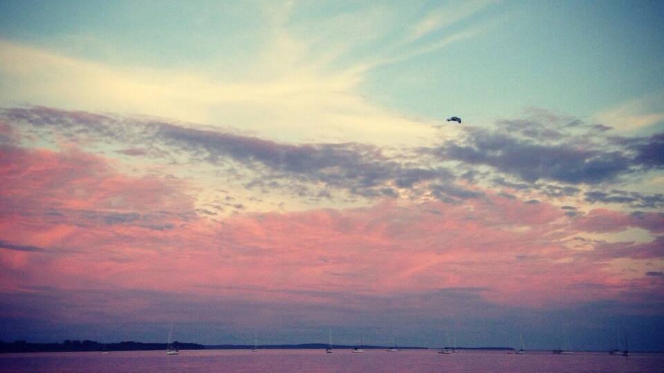 A sunset over a calm sea with boats and people on the shore.