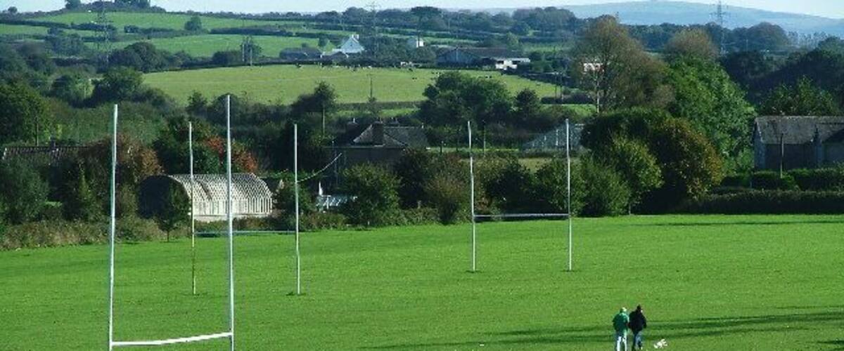 A grassy field with goalposts and two people playing a sport.