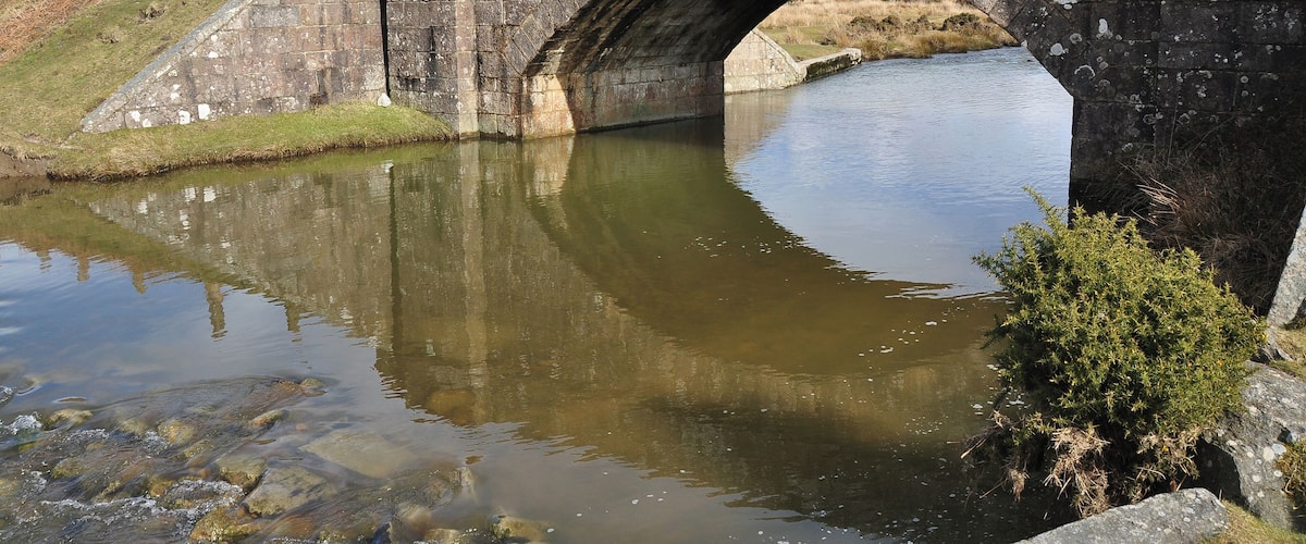 A stone bridge over a calm river with grassy banks and a clear sky.