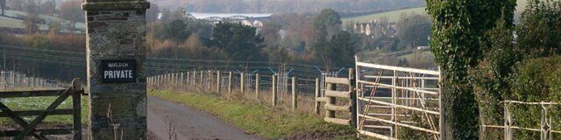 Gateway to Warleigh House. Situated by a gatehouse, Warleigh Lodge, these gates mark the start of a driveway to Warleigh House, over a kilometre away. This photograph looks west across the grid square towards the house and the River Tamar.