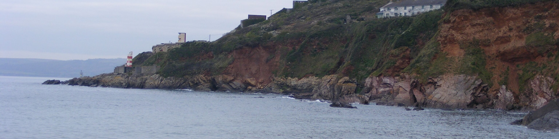 Paisagem costeira com uma praia arenosa, falésias rochosas e um farol.