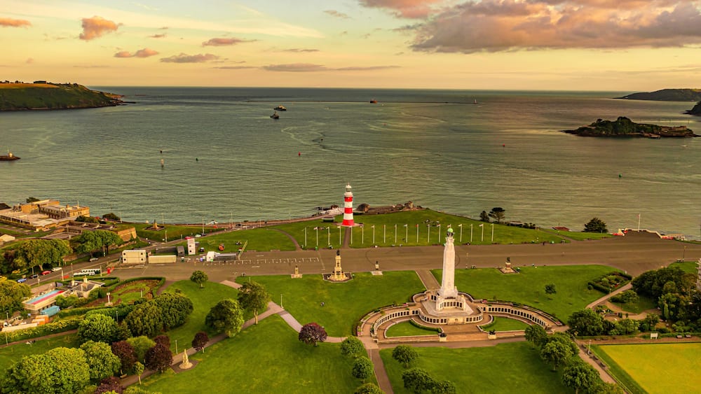 A coastal town with a prominent lighthouse, green park areas, and a clear view of the sea.