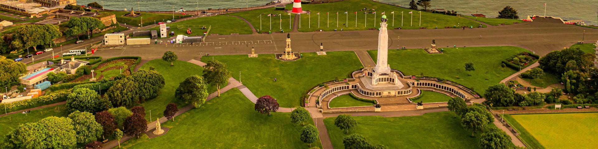 A coastal town with a prominent lighthouse, green park areas, and a clear view of the sea.