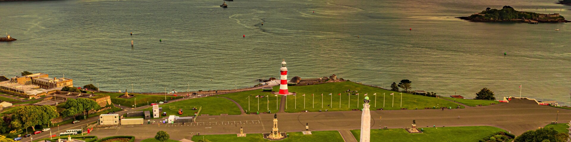 Un pueblo costero con un faro destacado, zonas verdes de parque y una vista despejada del mar.