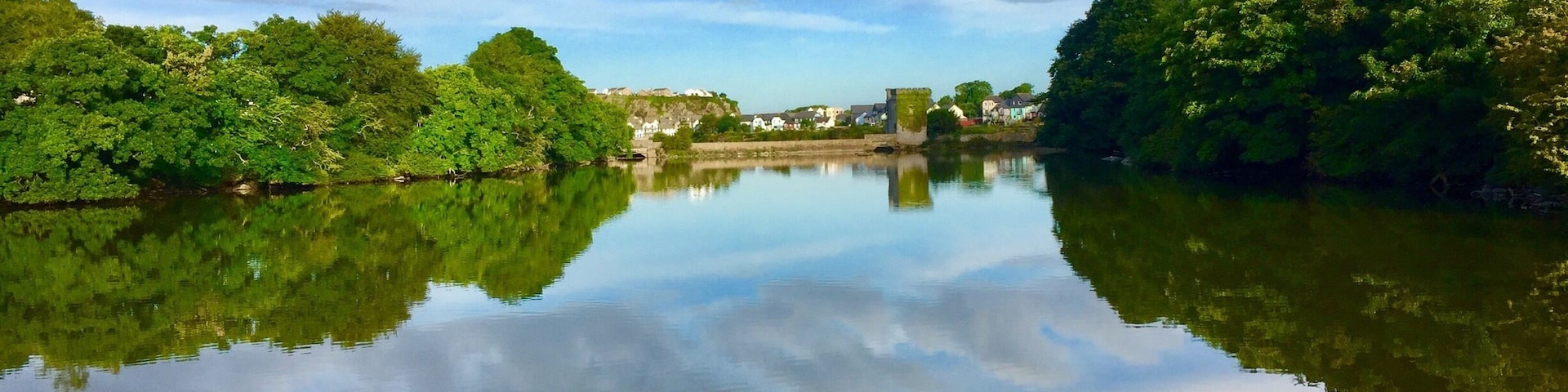 A calm river reflecting trees and a distant building.