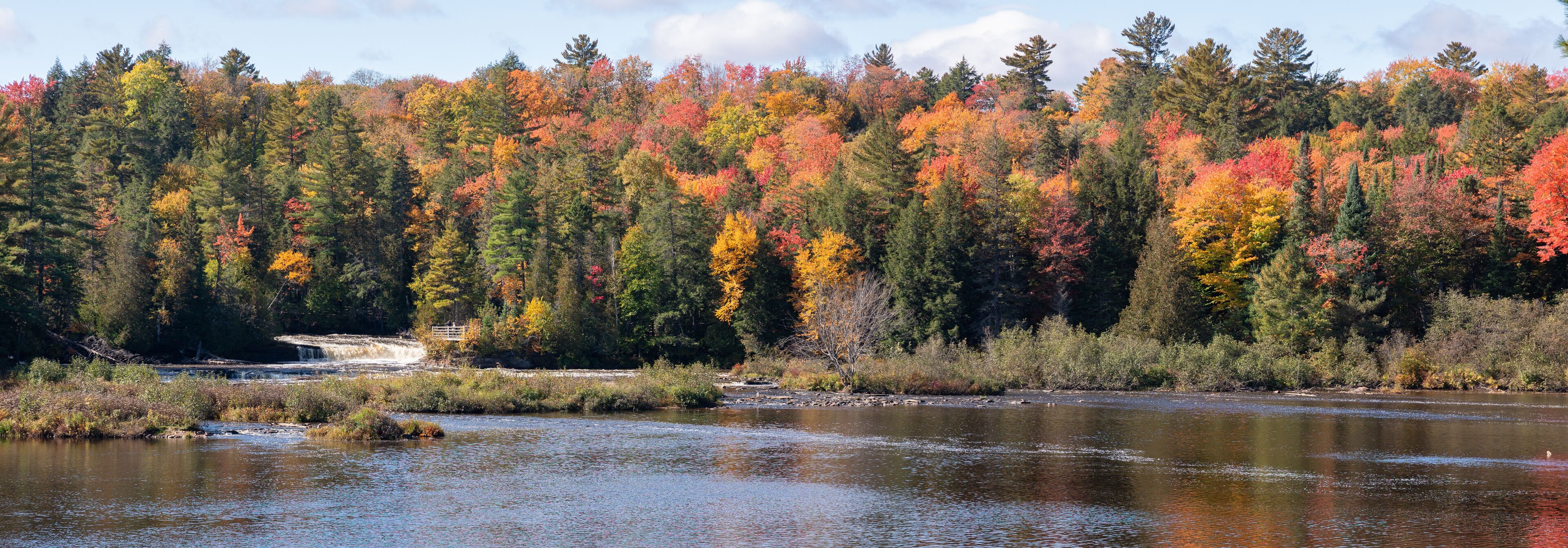 A river with autumn foliage, a small waterfall, and a bridge.
