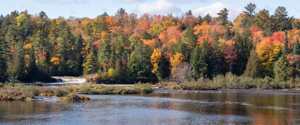 A river with autumn foliage, a small waterfall, and a bridge.