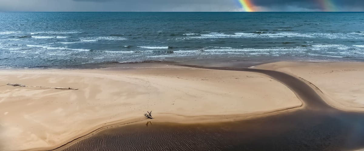 Colorful rainbow and rain over a sandy beach and estuary of small stream at the Baltic Beach, Europe