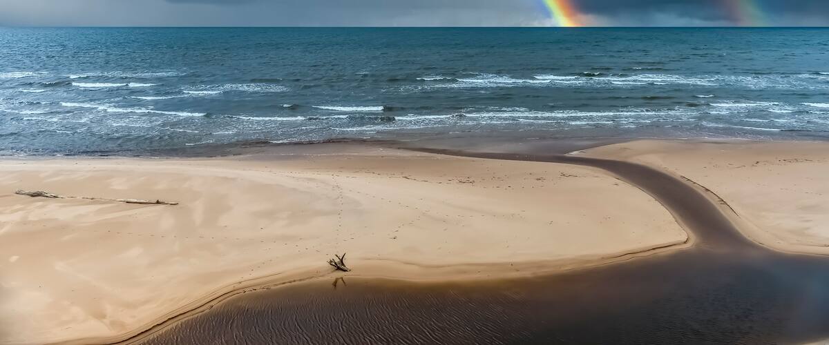 A beach with waves, a rainbow, and a dune.