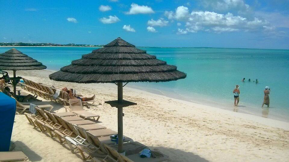 A beach with thatched umbrellas and lounge chairs.
