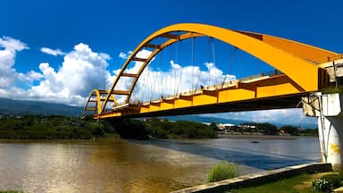 Uma ponte amarela sobre um rio, com montanhas ao fundo.