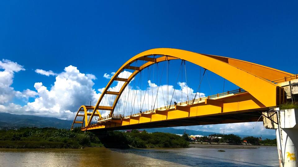A yellow bridge over a river with mountains in the background.