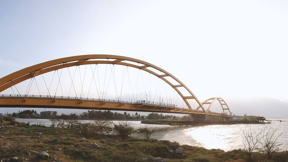 A large yellow bridge spanning a river with a mountainous backdrop.