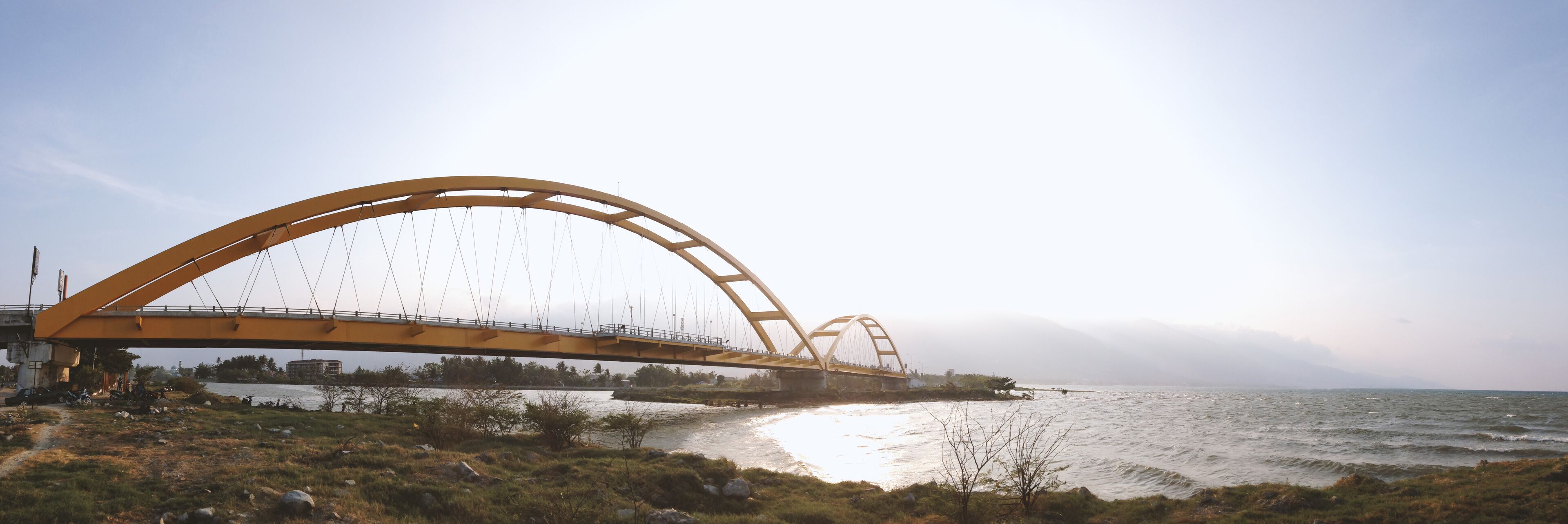 A large yellow bridge spanning a river with a mountainous backdrop.