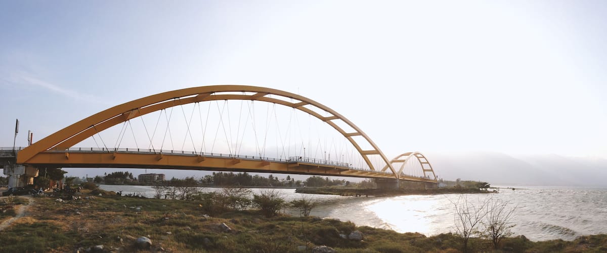 A large yellow bridge spanning a river with a mountainous backdrop.