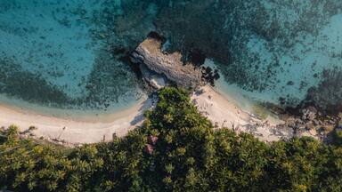 Uma praia tropical com águas turquesa cristalinas, um afloramento rochoso e palmeiras exuberantes.