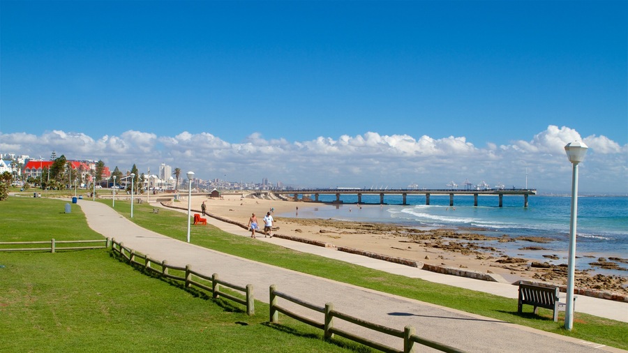 A coastal promenade with a beach, a pier, and a cityscape in the background.