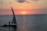 A sunset over a calm sea with a sailboat and a distant boat.