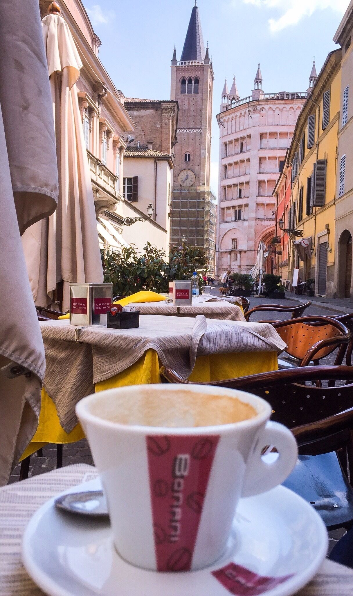 Ein Straßencafé mit einer Kaffeetasse, Tischen und einem Kirchturm im Hintergrund.