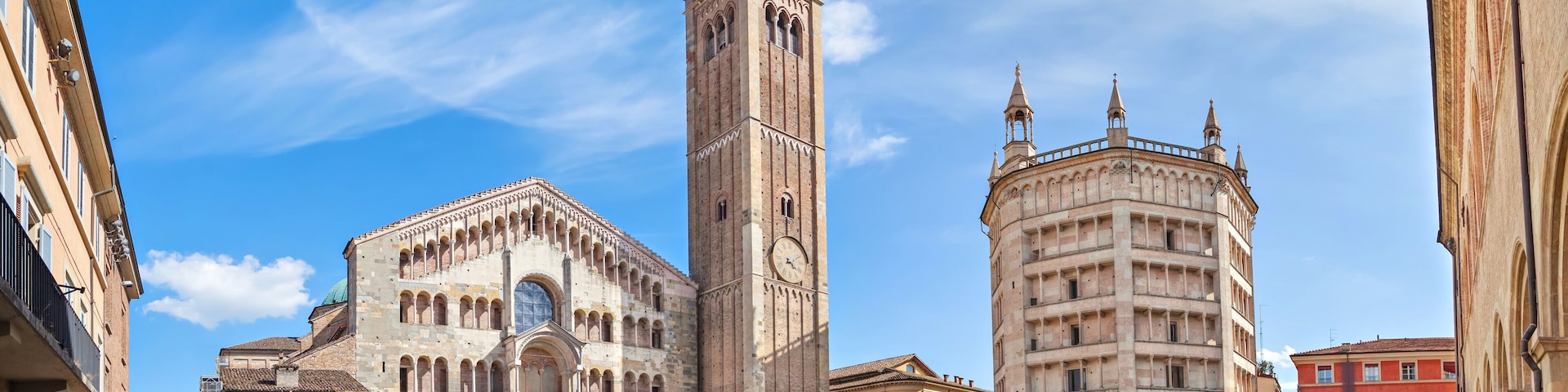 Uma praça histórica com uma igreja imponente, uma torre de sino alta e um edifício circular com cúpula.