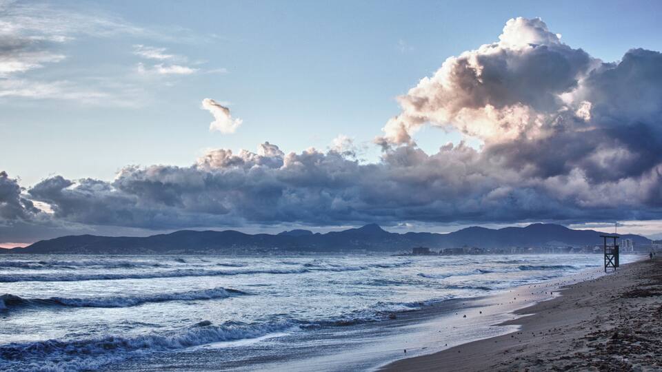 A beach with waves, a lifeguard tower, and mountains in the background.