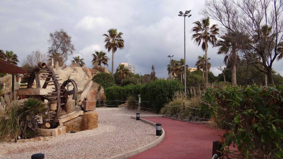 A park with a red pathway, palm trees, and a rock sculpture.