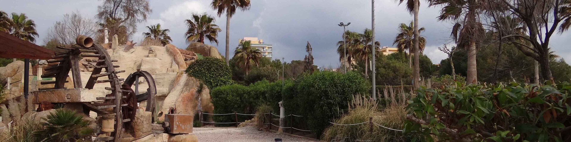 Un parque con un sendero rojo, palmeras y una escultura de roca.