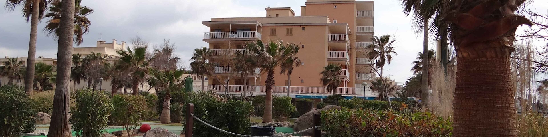 A golf course with a green path, palm trees, and a multi-story building in the background.