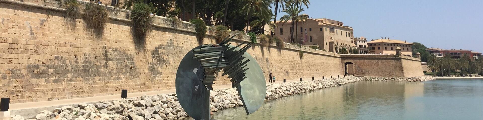 A historic cathedral with spires, palm trees, and a large sculpture by Salvador Dalí.
