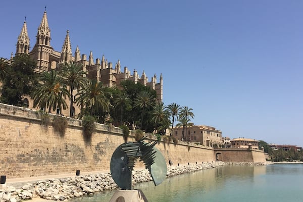 Eine historische Kathedrale mit Türmen, Palmen und einer großen Skulptur von Salvador Dalí.