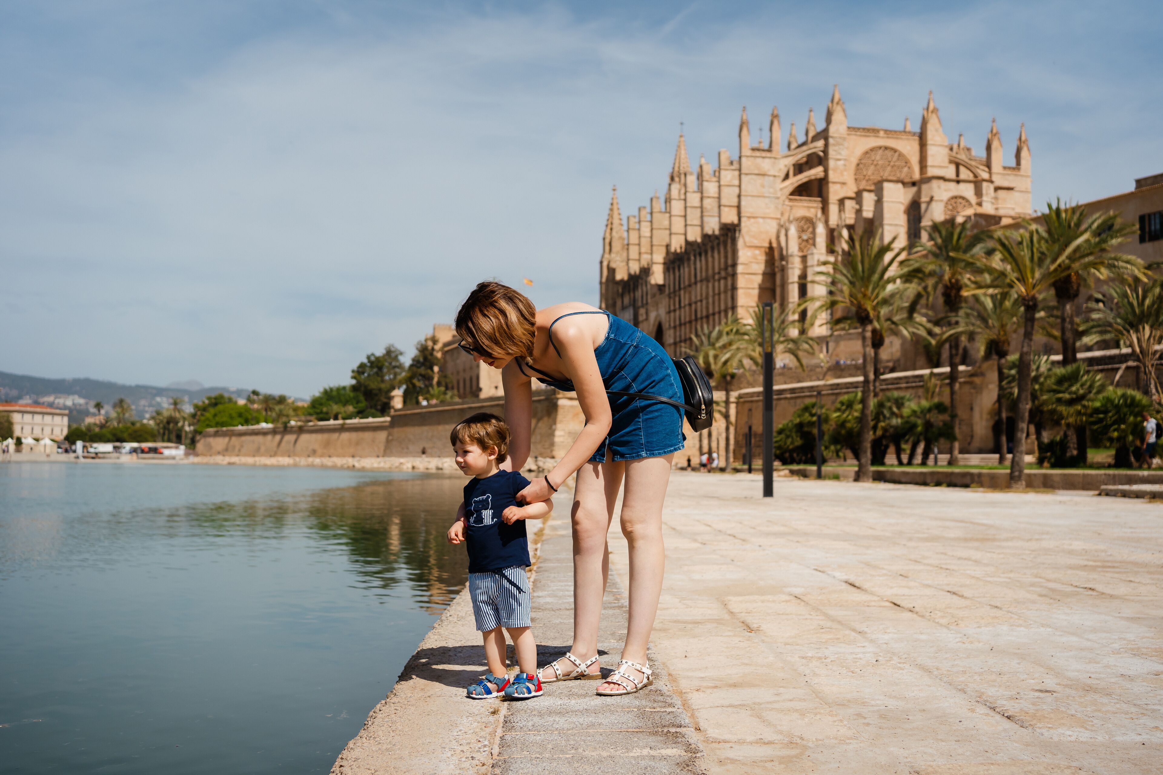 A woman and a child by a waterfront with a historic building in the background.