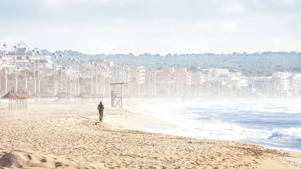 A beach with a lifeguard tower, umbrellas, and buildings in the background.