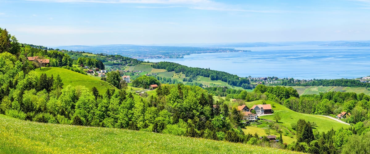 A lush green valley with rolling hills, a lake, and scattered houses.
