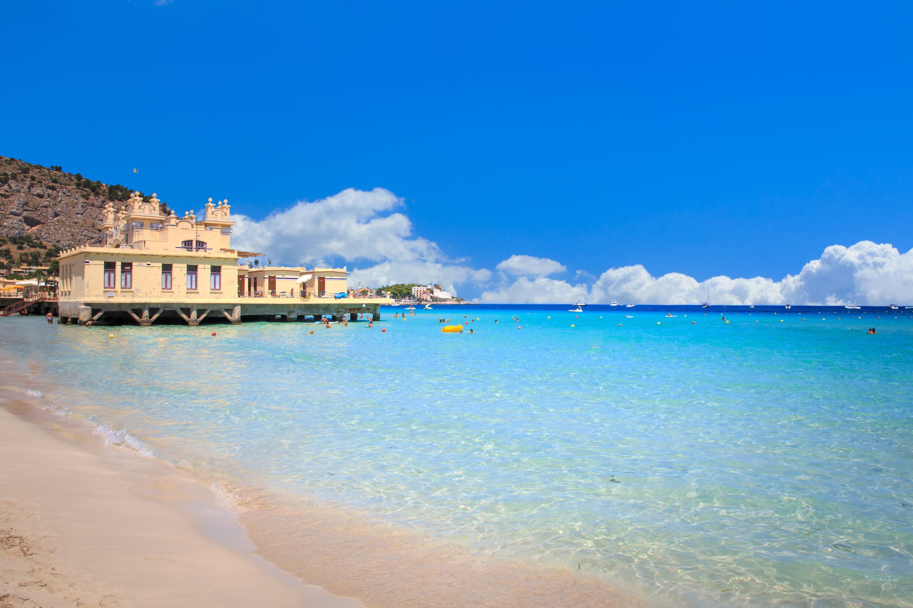 Una playa con agua turquesa cristalina, una orilla arenosa y un edificio de fachada blanca.