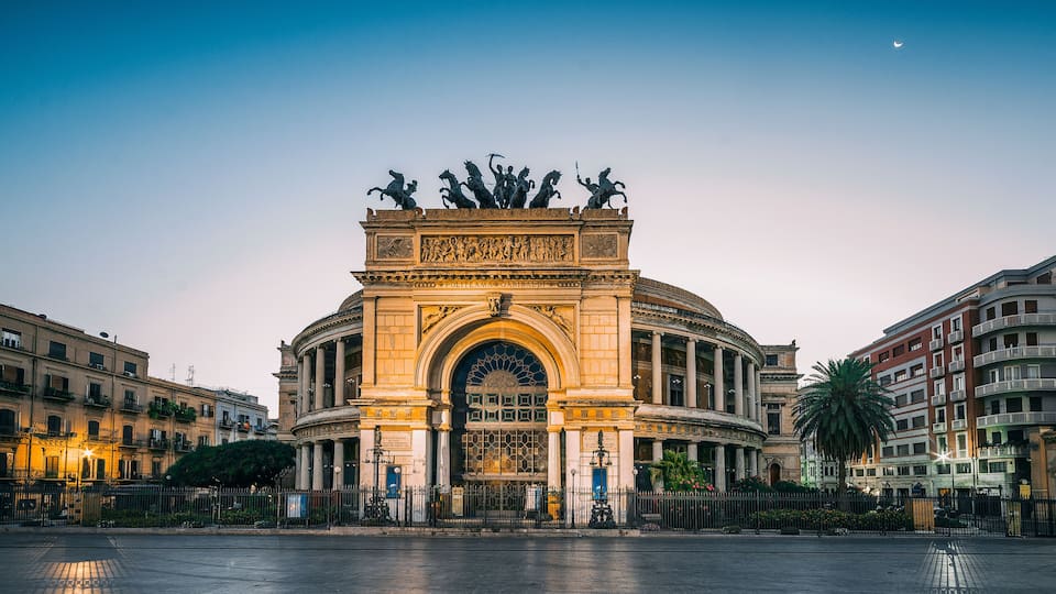 A grand archway with statues, surrounded by historic buildings and a clear sky.