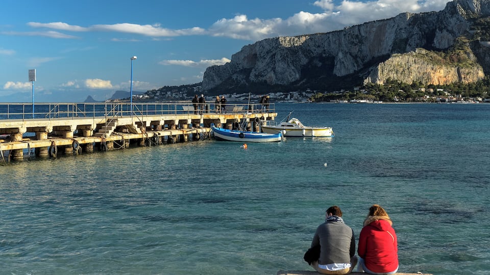 A pier extending into calm waters with a rocky cliff in the background.