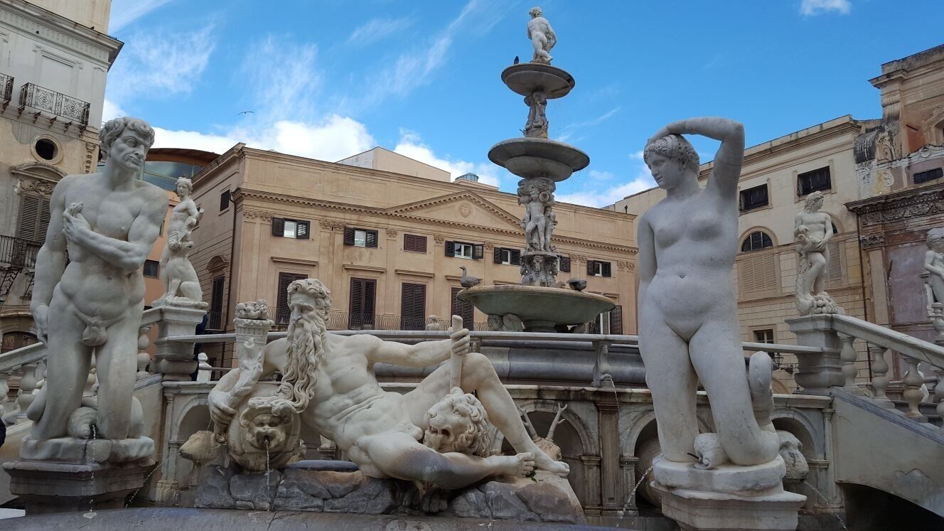 Uma fonte clássica com estátuas, rodeada por edifícios históricos.