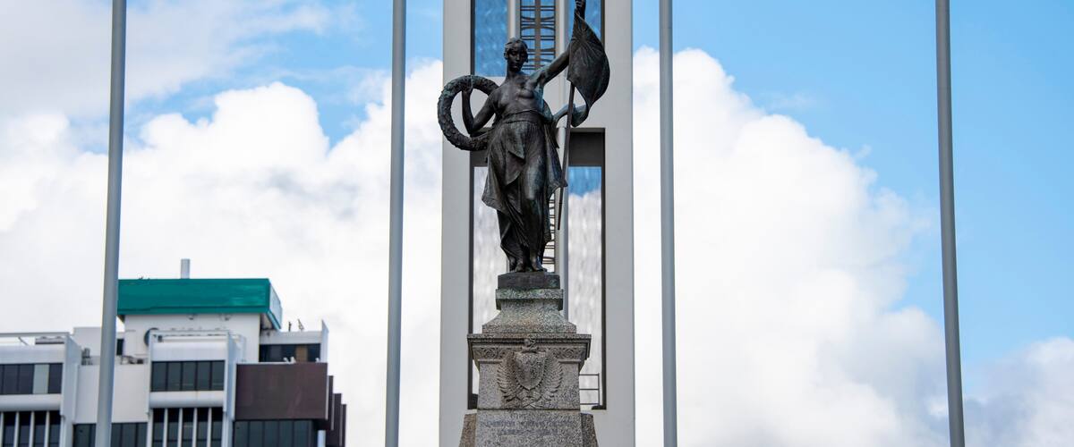 Een standbeeld van een figuur met een vlag, met een gebouw en vlaggen op de achtergrond.