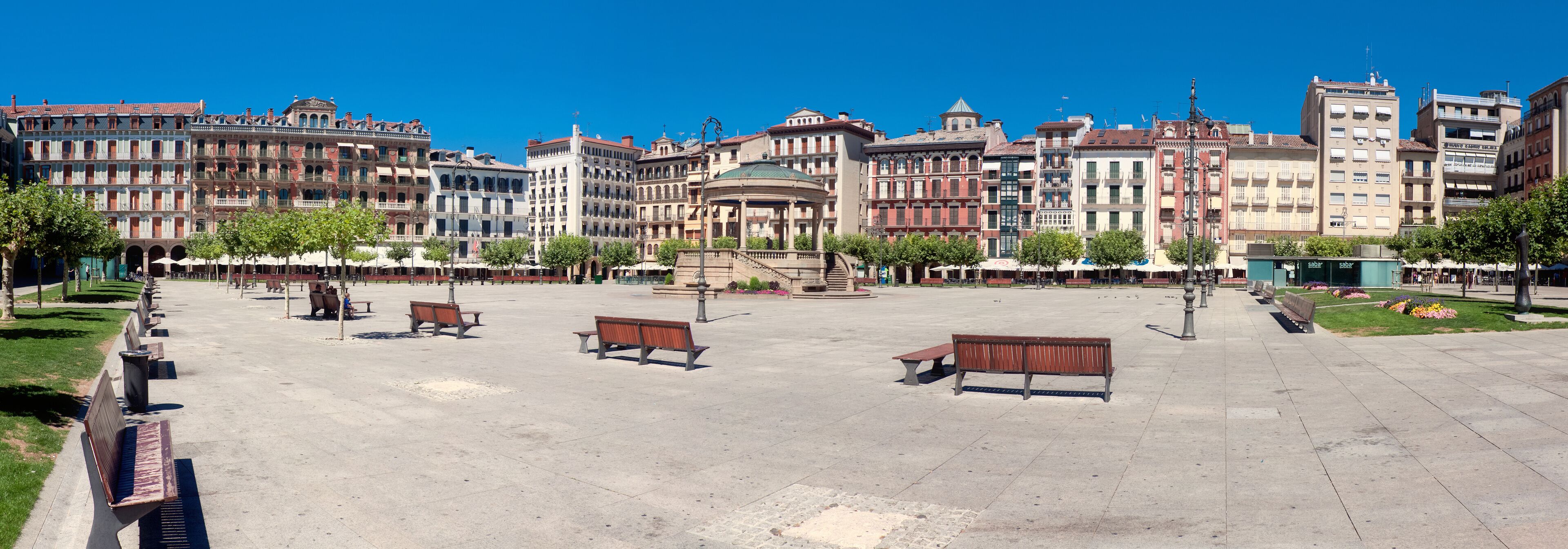 A spacious plaza with benches and trees, surrounded by historic buildings with varied architecture.