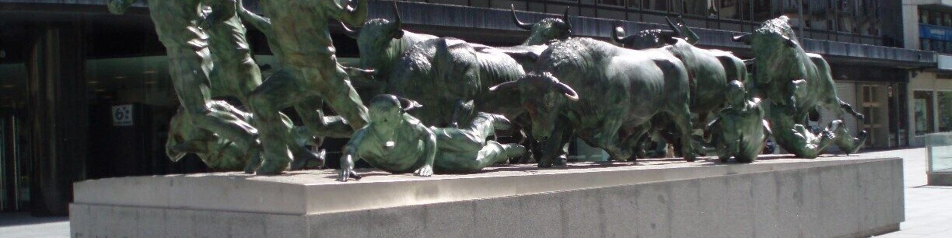 Escultura de bronce de un torero en acción, titulada 'ENCIERRO', frente a la fachada de un edificio moderno.
