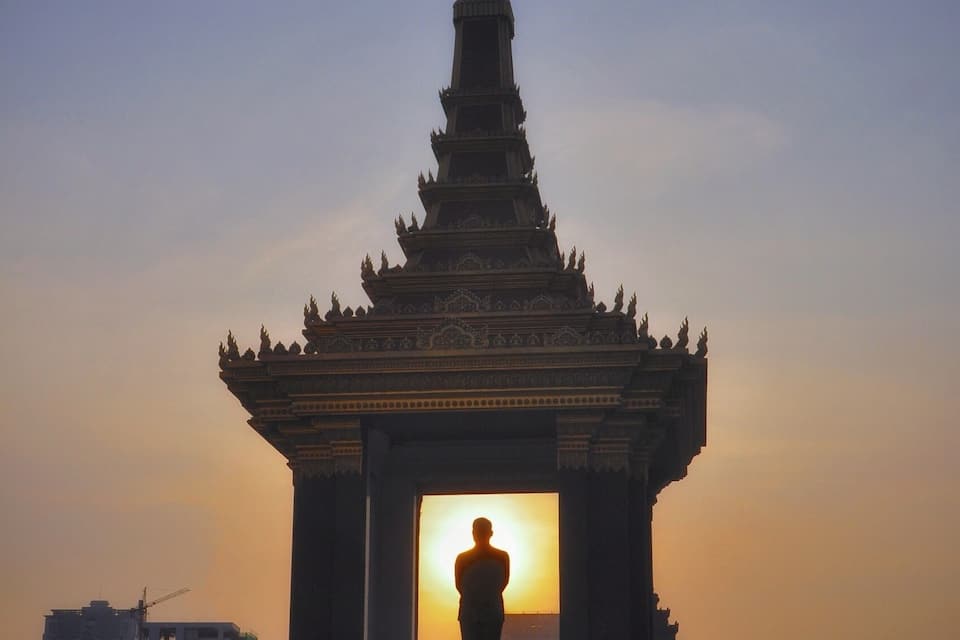 A traditional Thai temple with a statue in front, set against a sunset sky.