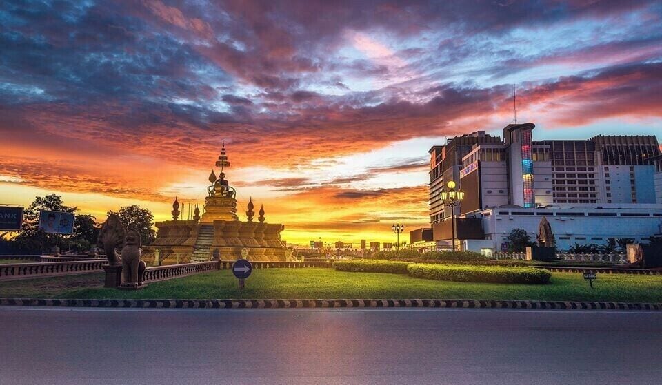 A sunset over a cityscape with a prominent golden pagoda and modern buildings.