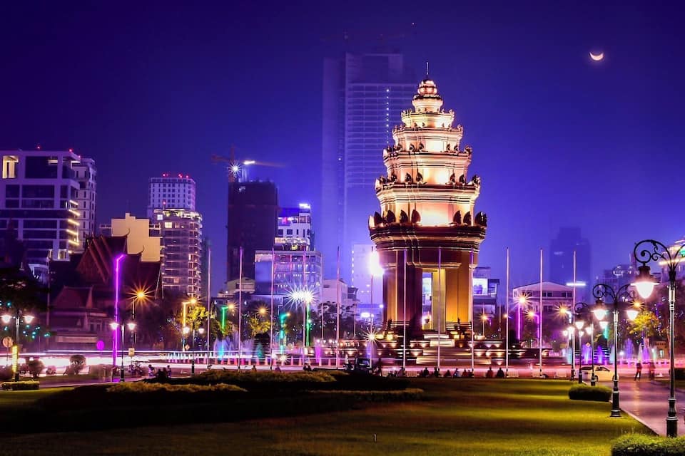 Un paisaje urbano nocturno con una torre iluminada destacada y edificios modernos.
