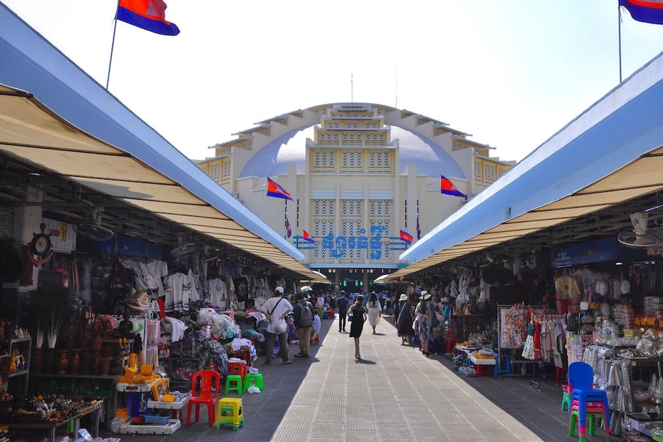 A bustling market with stalls selling various goods, a central archway, and flags.
